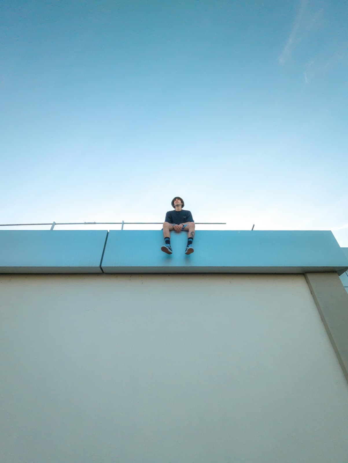 A man sitting on a rooftop ledge looking up at a clear blue sky
